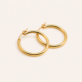 Naut & Chain medium hoop earrings with a sleek circular design, made of polished metal, hanging against a neutral background.