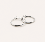 A pair of polished silver hoop earrings with post-back closures, displayed on a clean, solid, warm off-white background.