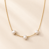 A delicate gold chain necklace featuring three irregular white baroque pearls spaced along the chain, displayed on a soft beige background.
