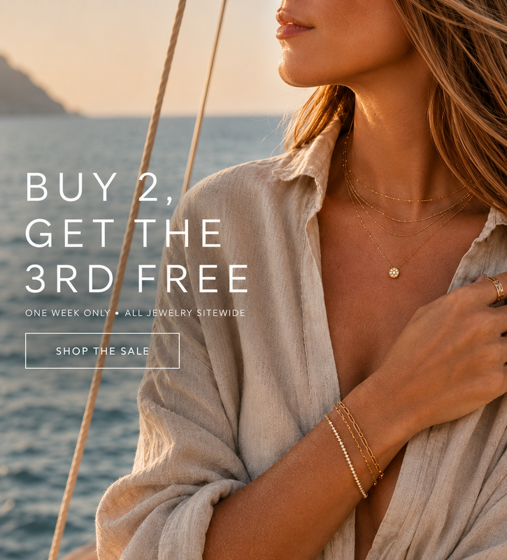 A woman on a boat wearing layered gold necklaces and bracelets, with a linen shirt against a warm ocean sunset background. Large promotional text reads 'BUY 2, GET THE 3RD FREE' and 'SHOP THE SALE'.